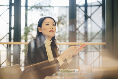 Confident businesswoman holding mobile phone sitting at cafeteria in office