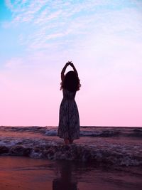 Rear view of woman standing by sea against sky during sunset