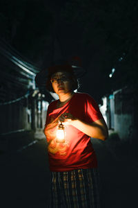 Woman holding illuminated while standing outdoors at night