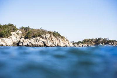 Surface level of rocks by sea against clear sky