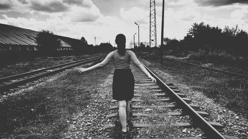 Rear view of woman walking on railroad track against cloudy sky during sunset