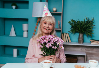 Portrait of smiling senior woman holding flowers at home