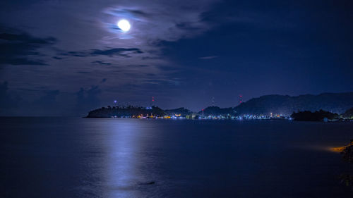 Illuminated city by sea against sky at night