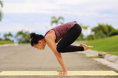 Side view of young woman exercising on mat at park