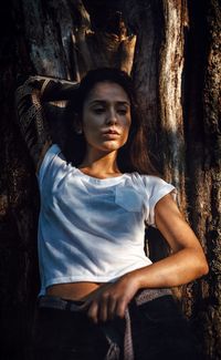 Thoughtful woman leaning on tree trunk