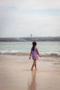 Rear view of woman standing at beach against sky