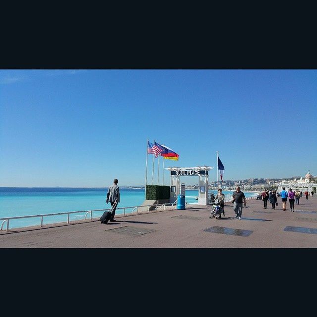 clear sky, sea, copy space, horizon over water, transportation, blue, large group of people, men, leisure activity, beach, lifestyles, water, sunlight, person, transfer print, mode of transport, travel, flag, day