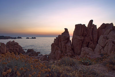 Rock formations on shore against sky during sunset