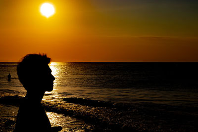 Silhouette man at sea against sky during sunset