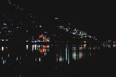 Illuminated buildings by river against sky at night