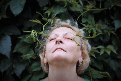 Close-up of senior woman standing with closed eyes by plants