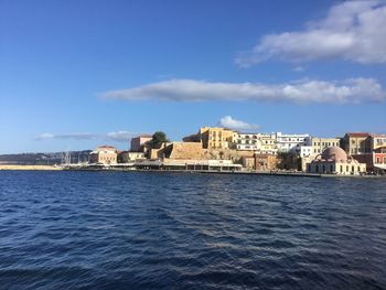 Sea by buildings against blue sky