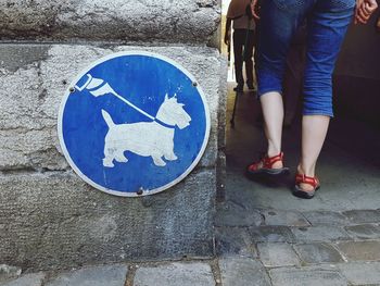 Low section of woman walking by dog sign on wall