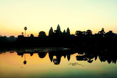 Silhouette buildings by lake against sky during sunset