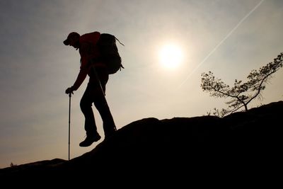 Man hiker make down step, legs in boots and poles. sunny mountain peak rock. small pine bonsai tree 