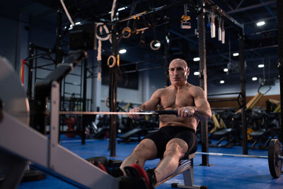 Powerful aged man exercising on rowing machine