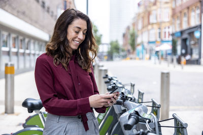 Smiling businesswoman using mobile phone to rent bicycle for commuting in city