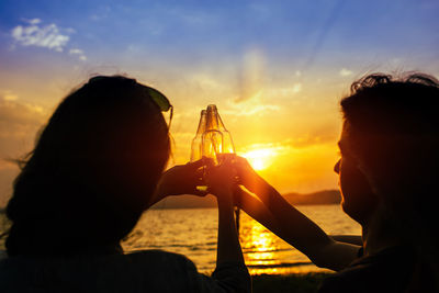 Rear view of a man drinking glass against sunset sky