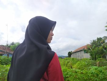 Young woman wearing hijab standing against plants