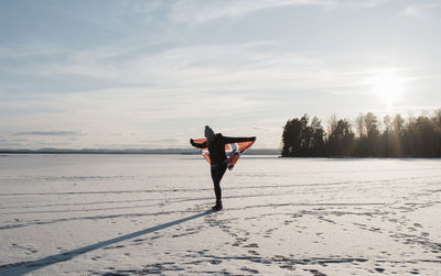 Woman walking across a frozen lake holding a norwegian flag at sunset