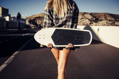 Midsection of woman with skateboard standing on road