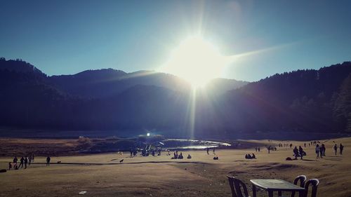 Group of people on beach against bright sun