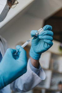 Doctor wearing protective glove preparing covid-19 dose syringe while at clinic