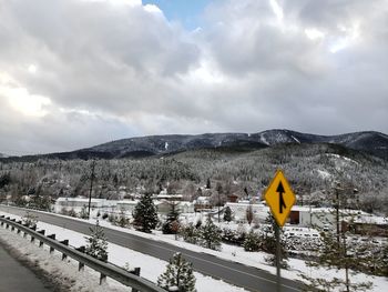 Road sign on snow covered mountain against sky