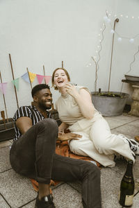 Happy young woman laughing while sitting with male friend at party in balcony