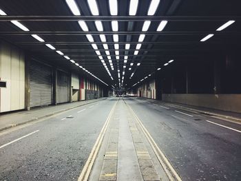 Empty illuminated road amidst shops