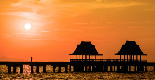 Silhouette wooden posts in sea against orange sky