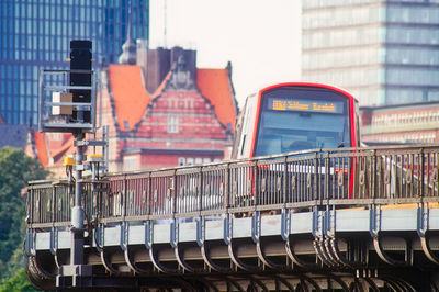 Metallic structure by building and train in city against sky