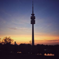 Silhouette communications tower and buildings against sky during sunset