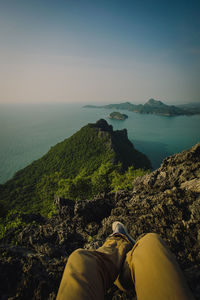 Low section of person on rock by sea against sky