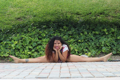 Portrait of woman doing splits on floor against plants