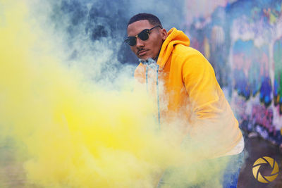 Full length of man holding distress flare while crouching on wet footpath