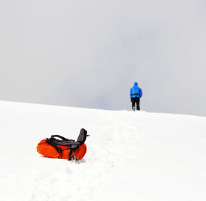 Rear view of hooded person walking on snow covered landscape against sky