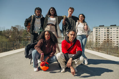 Portrait of multiracial male and female friends posing together on railroad station platform during sunny day