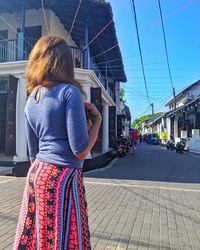 Rear view of woman standing against sky in city