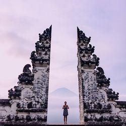 Portrait of smiling young woman with hands clasped while standing at old ruins