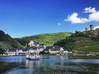 Houses by river moselle and buildings against blue sky