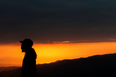 Silhouette man standing against orange sky during sunrise