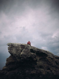 Low angle view of man sitting on rock against sky