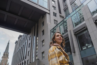 Happy business woman in a yellow coat goes to a business center in a big city.