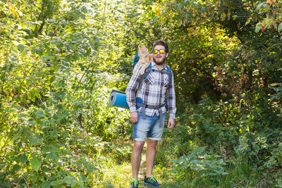 Full length portrait of young man standing against trees