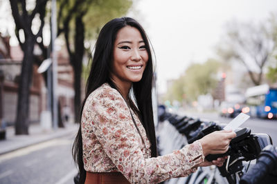 Smiling woman renting bicycle through credit card in city