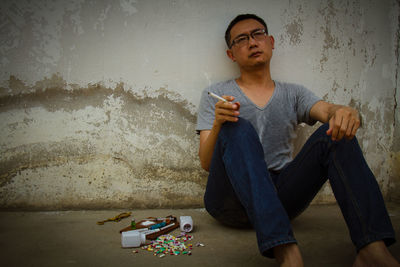 Man holding marijuana joint while sitting against wall