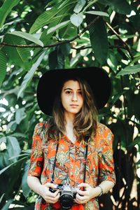 Portrait of young woman standing against tree