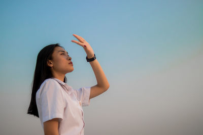 Young woman shielding eyes standing against sky during sunset