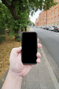 Cropped hand of man holding smart phone on sidewalk in city